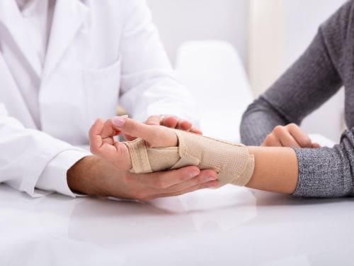 Anche le fratture sono causa del dolore alle mani: scopri perchè! Donna con tutore alla mano in visita dal medico
