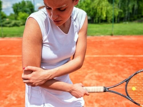 Scopri quali sono le principali cause che possono scatenare la tendinite! Donna gioca a tennis e si tocca il gomito a causa di un dolore
